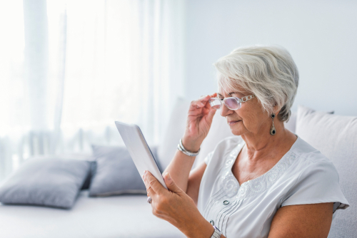 Elderly woman struggling to read tablet while lowering glasses