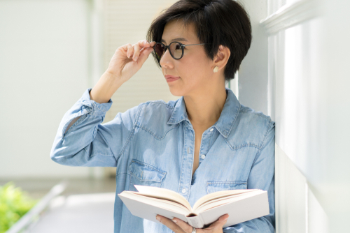 woman holding eyeglasses in one hand and a book in the other hand