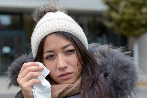 A woman is squinting while holding a tissue near her eyes