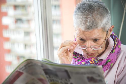Older woman lowering glasses while struggling to read due to cataracts
